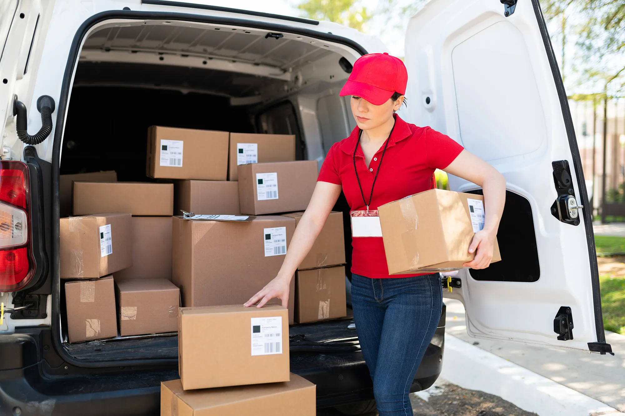 Female van driver in red uniform unloading boxes from the back of a small white van